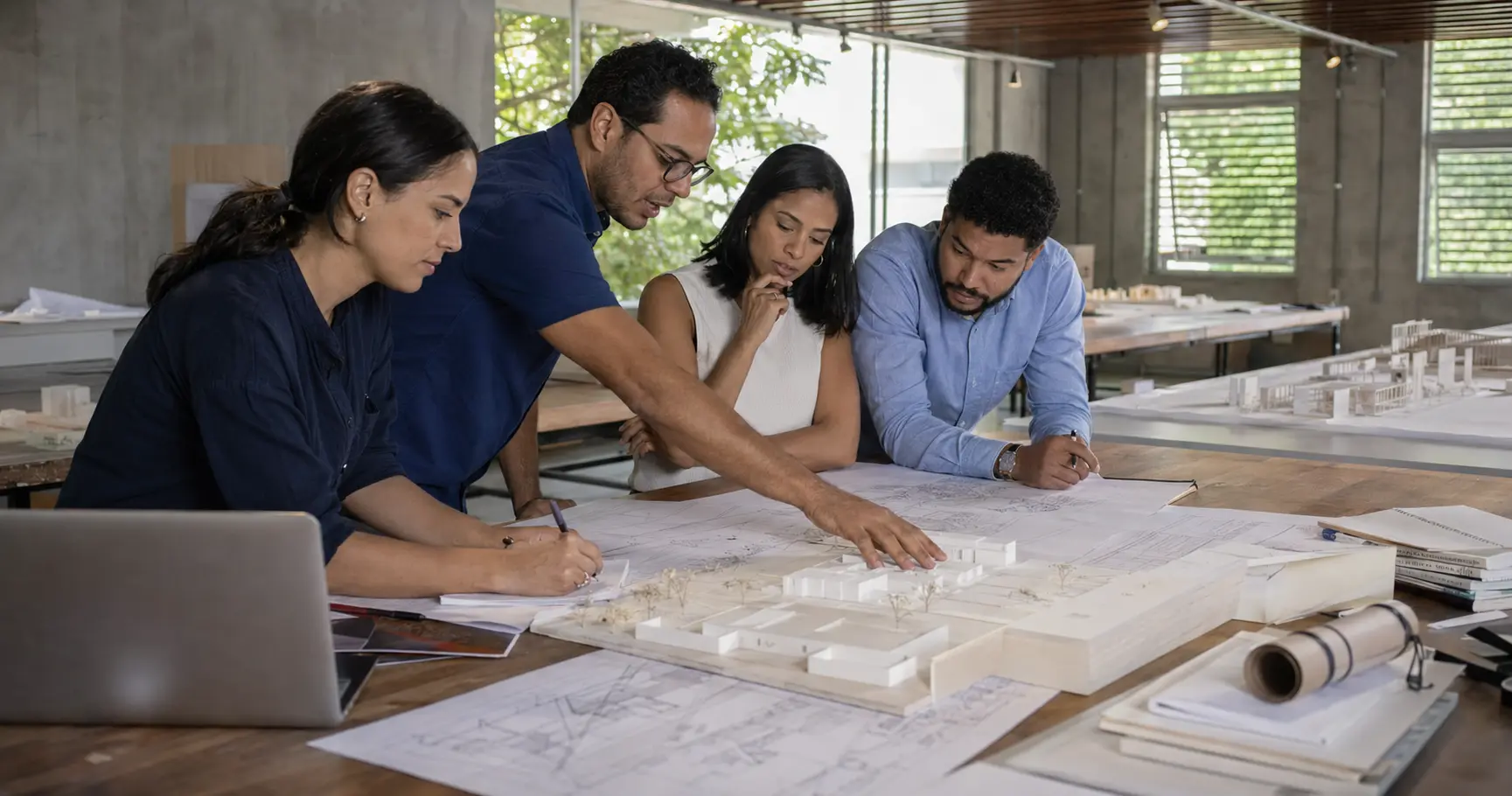 Profesionales colaborando alrededor de planos y un modelo arquitectónico